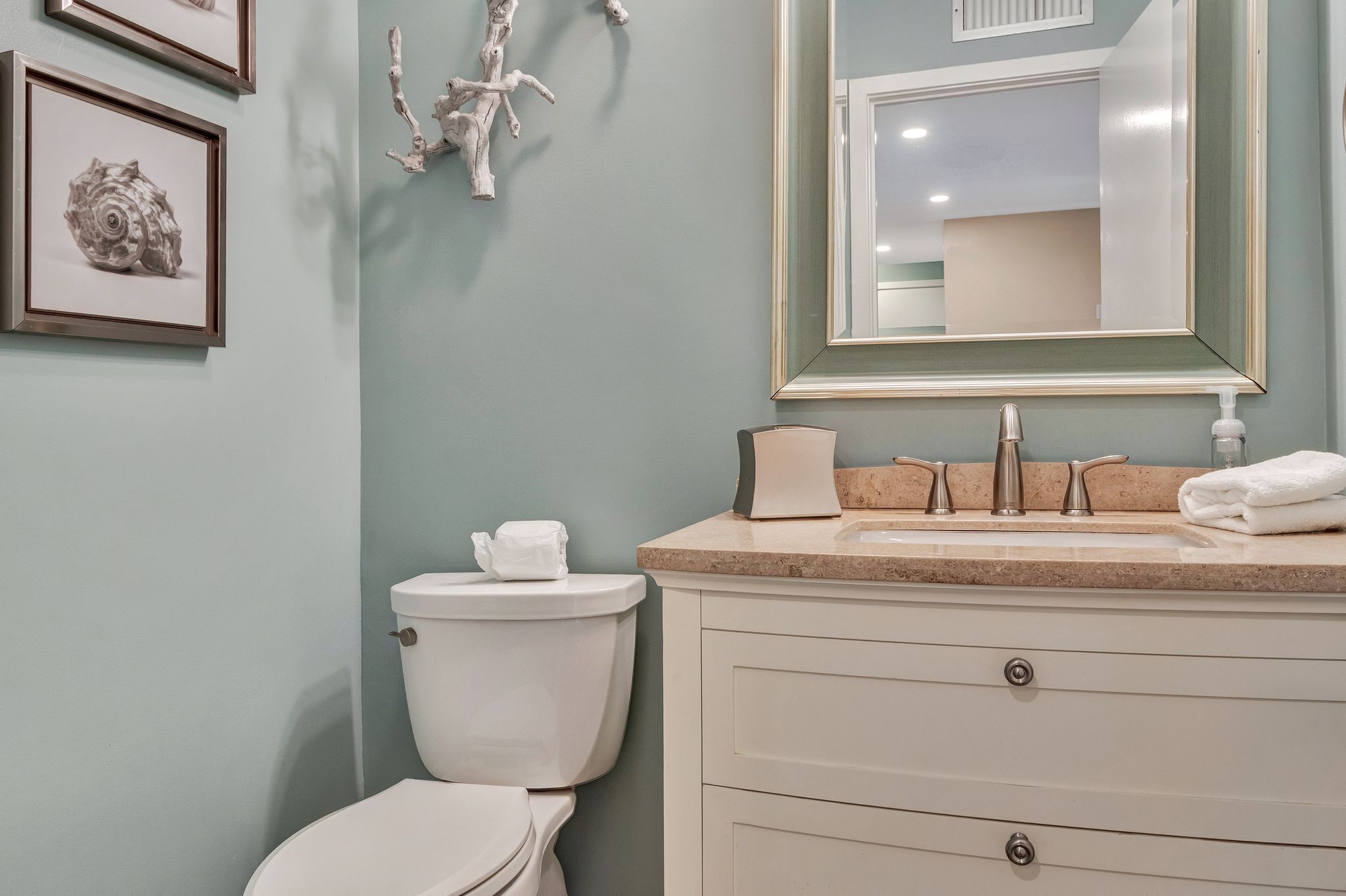 A bathroom with a toilet, sink, and mirror. There are framed pictures on the wall.