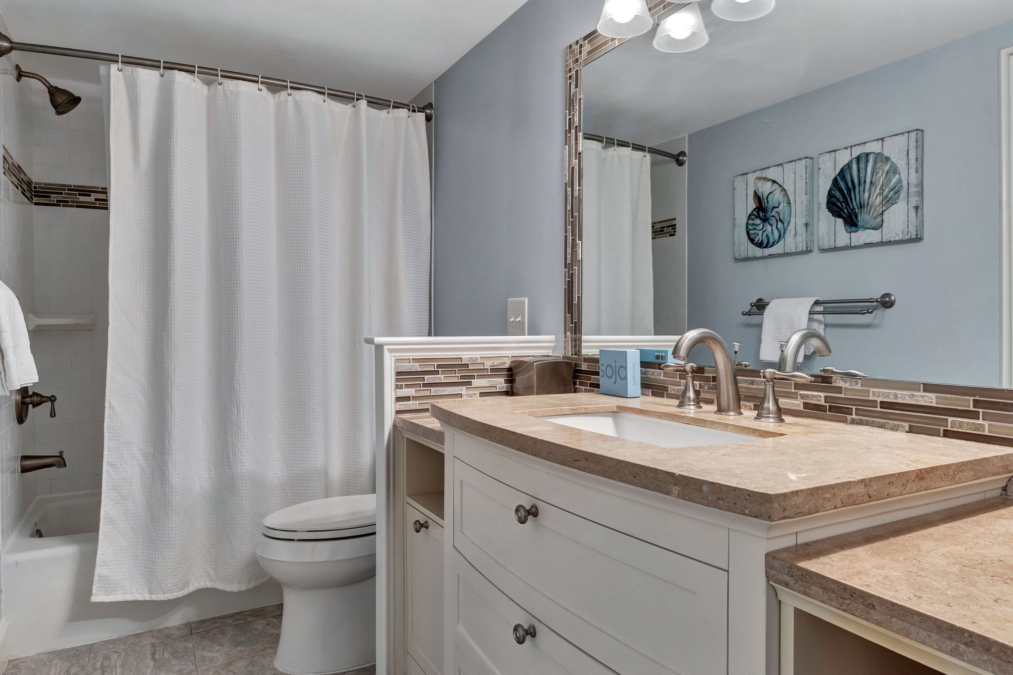 A bathroom with a shower curtain, a toilet, a sink with a mirror, and a towel rack.