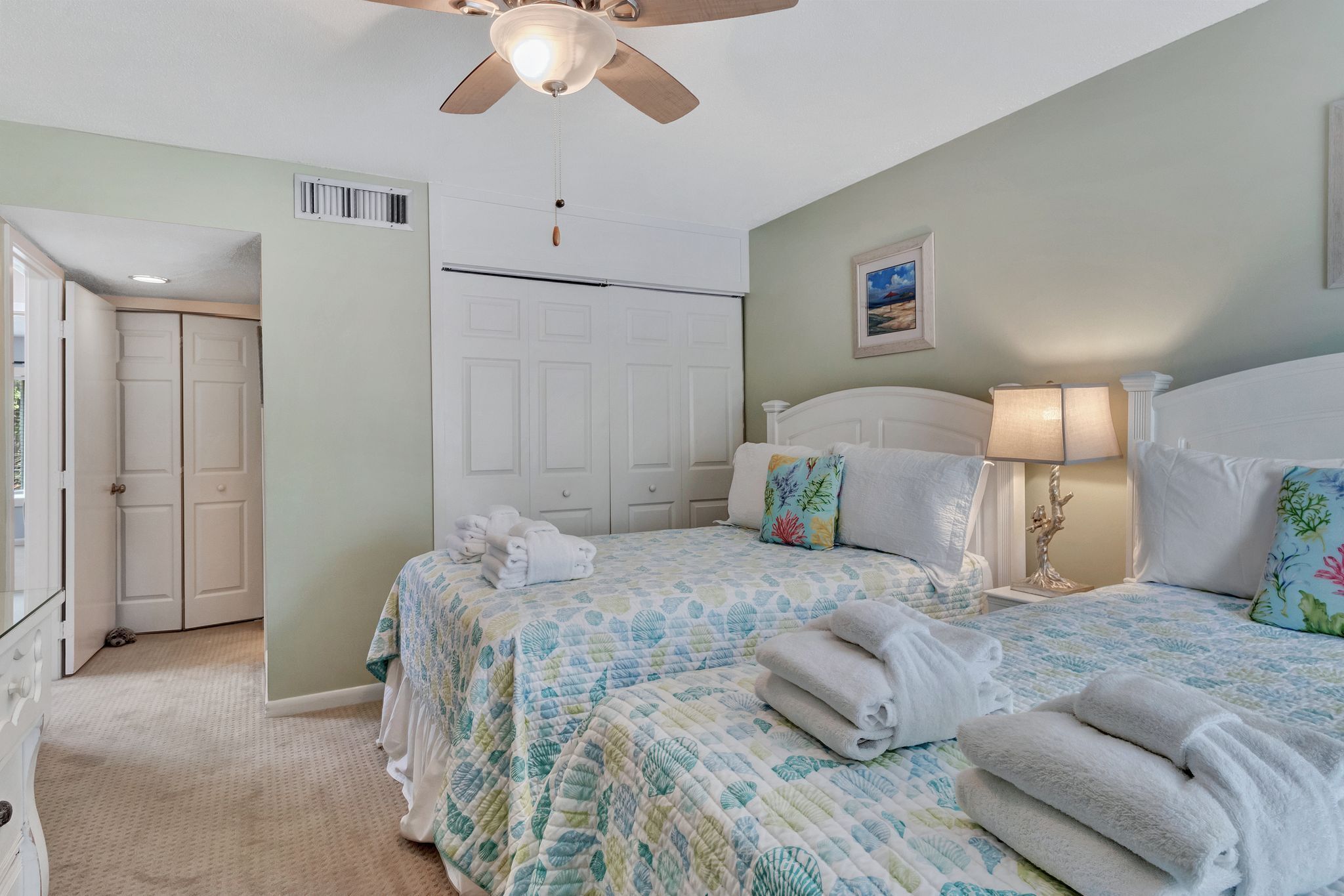 A bedroom with two beds, a ceiling fan, a nightstand with a lamp, and a door leading to a closet.