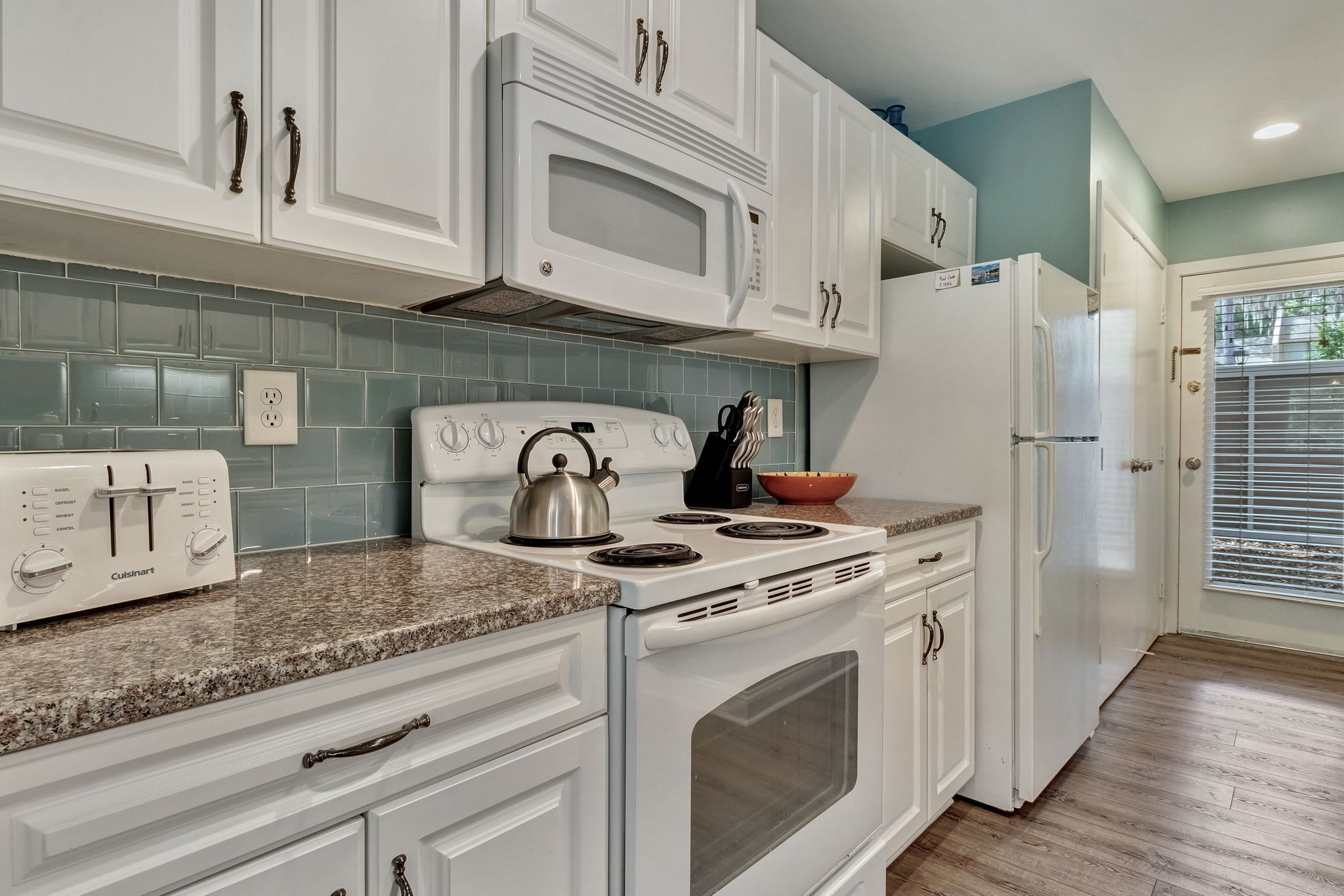 A kitchen with white cabinets, a white stove, a microwave, and a refrigerator.