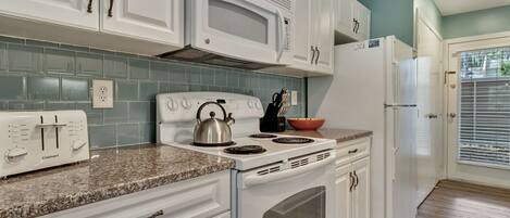 A kitchen with white cabinets, a white stove, a microwave, and a refrigerator.