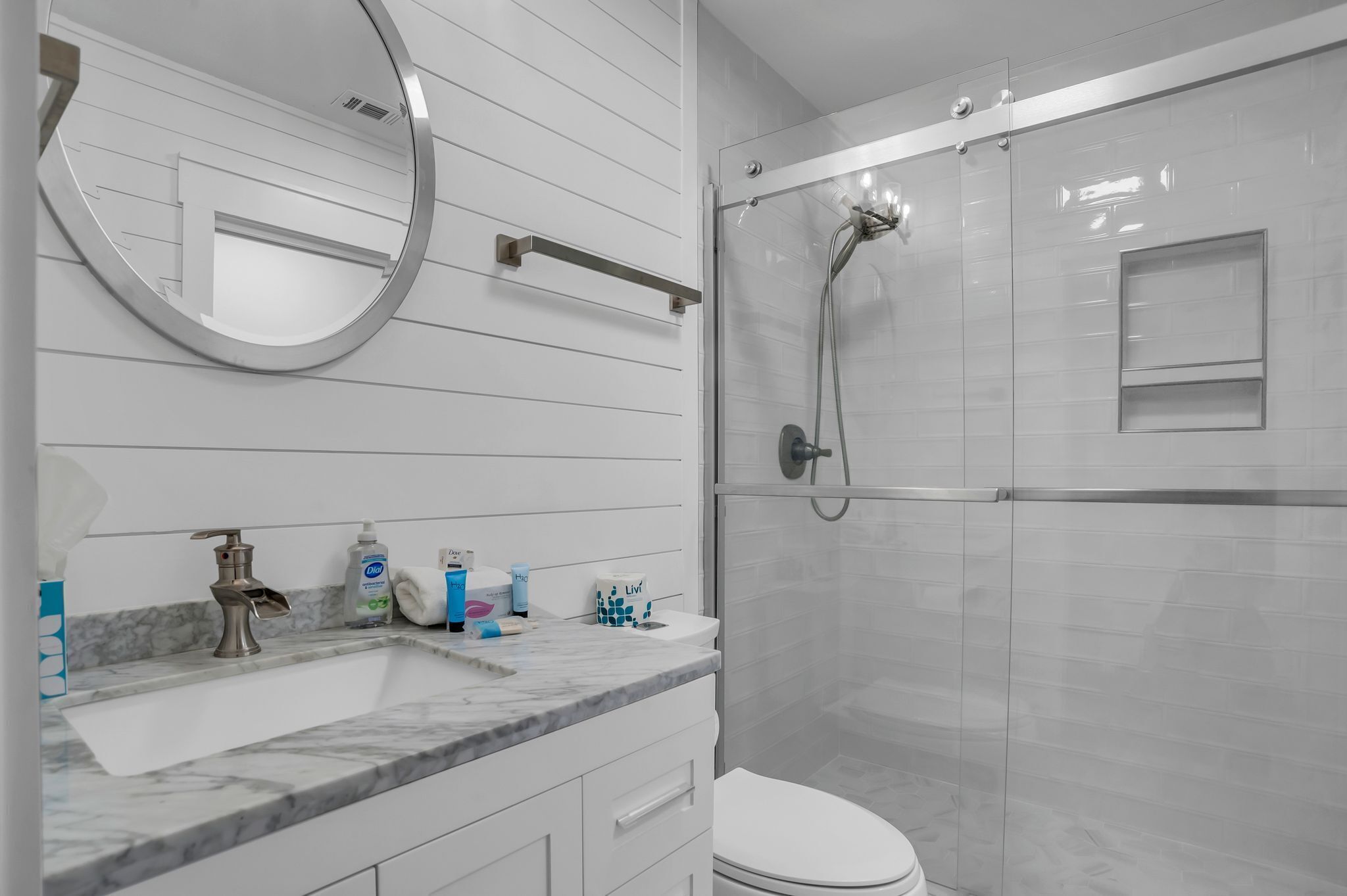 Un baño moderno con lavamanos de mármol, un espejo redondo, ducha con cerramiento de vidrio y un inodoro.