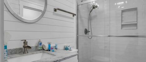 Un baño moderno con lavamanos de mármol, un espejo redondo, ducha con cerramiento de vidrio y un inodoro.