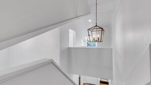 A white interior with a geometric staircase and a hanging light fixture. - 26 Muirfield Road at The Sea Pines Resort (Hilton Head Island)