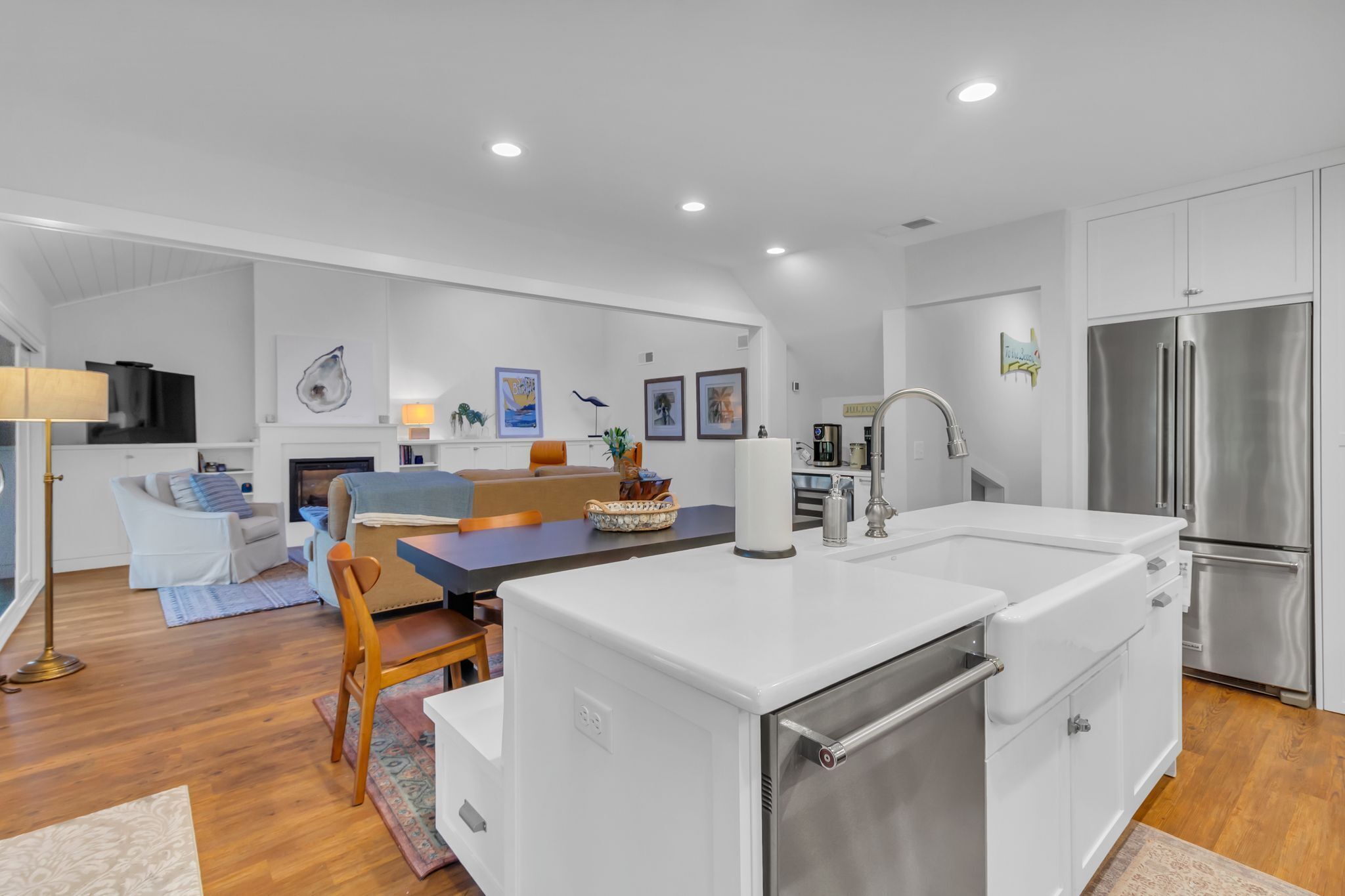A modern kitchen with white cabinetry, a stainless steel refrigerator, and a dining area with a blue table and chairs.
