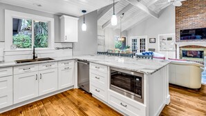 A modern kitchen with white cabinetry, a large island with an oven, and a dining area with a brick fireplace.