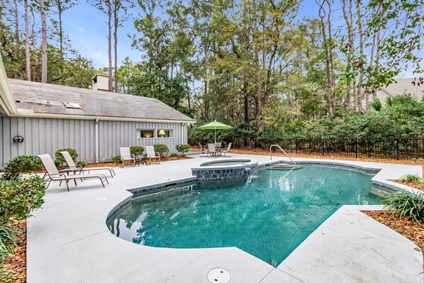 A swimming pool with a curved design, surrounded by lounge chairs and a small building with a sloped roof. - 67 Forest Drive at The Sea Pines Resort (Hilton Head Island)