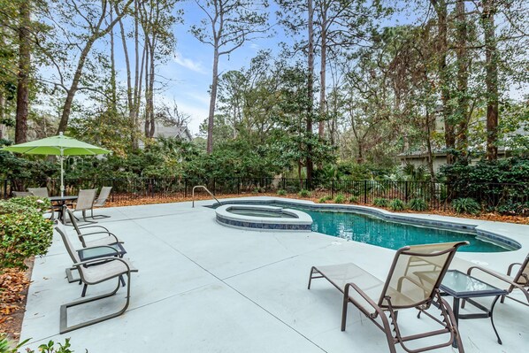 A backyard with a swimming pool, lounge chairs, and a table with an umbrella. - 67 Forest Drive at The Sea Pines Resort (Hilton Head Island)