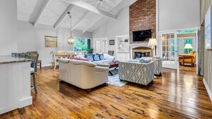 A spacious living room with a high ceiling, wooden flooring, a fireplace, and a television.