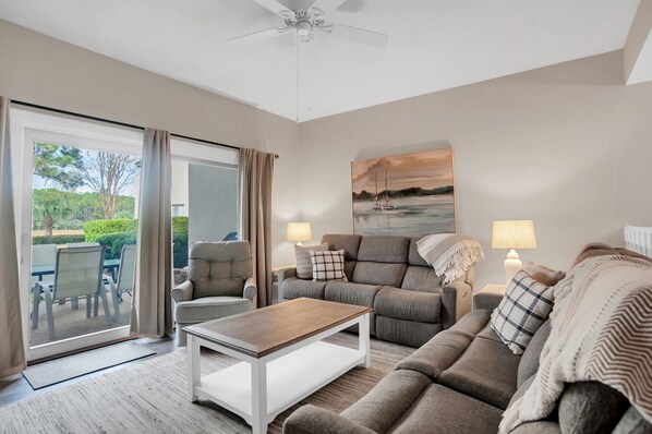 A modern living room with a sofa, a coffee table, and a painting of a sunset over water. - 264 Stoney Creek Villa at The Sea Pines Resort (Hilton Head Island)