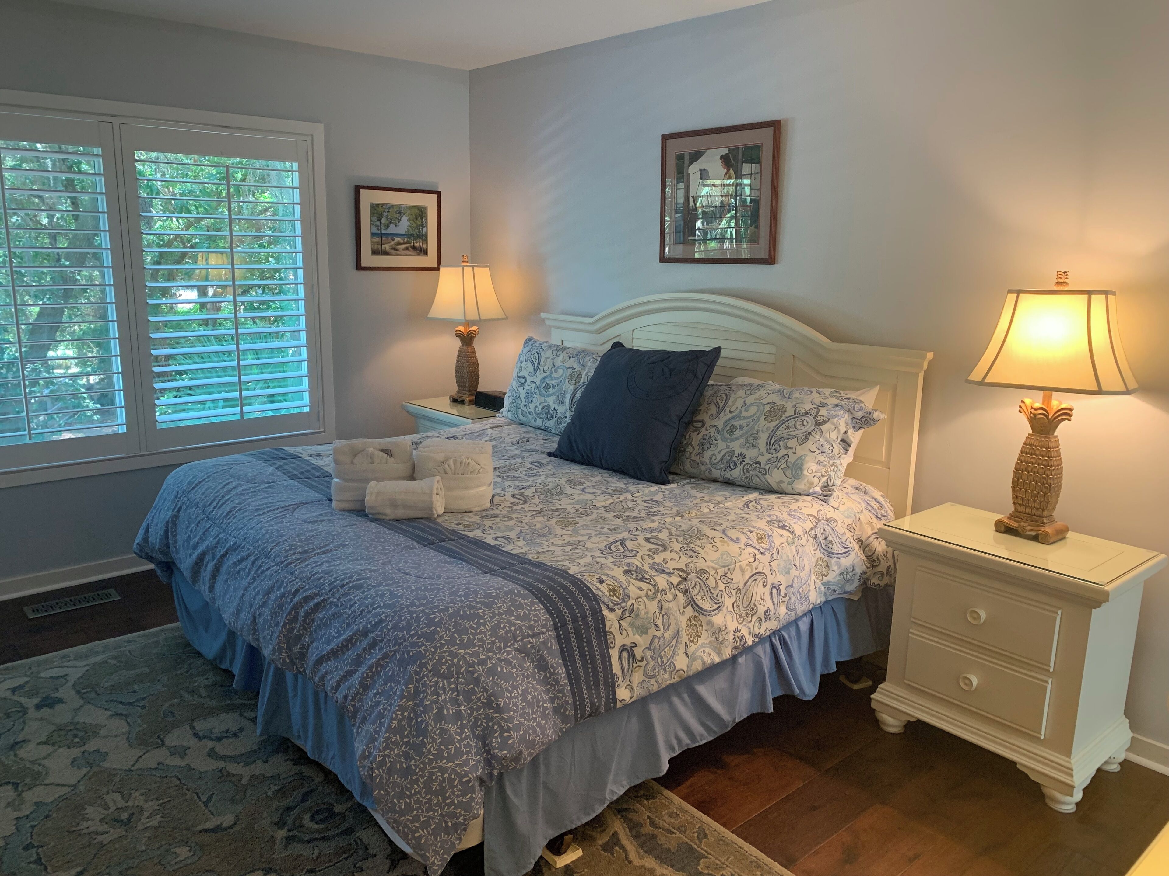 A bedroom with a bed, two nightstands, a window with blinds, and two wall-mounted lamps.