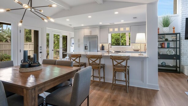 A modern kitchen with white cabinets, a central island, and a dining area with a wooden table and chairs. - 6966 Fairway One at The Sea Pines Resort (Hilton Head Island)