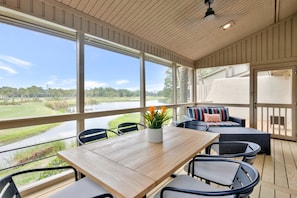 An outdoor deck with a wooden table and chairs, a cushioned seating area, and a view of a lake and golf course. - 6966 Fairway One at The Sea Pines Resort (Hilton Head Island)