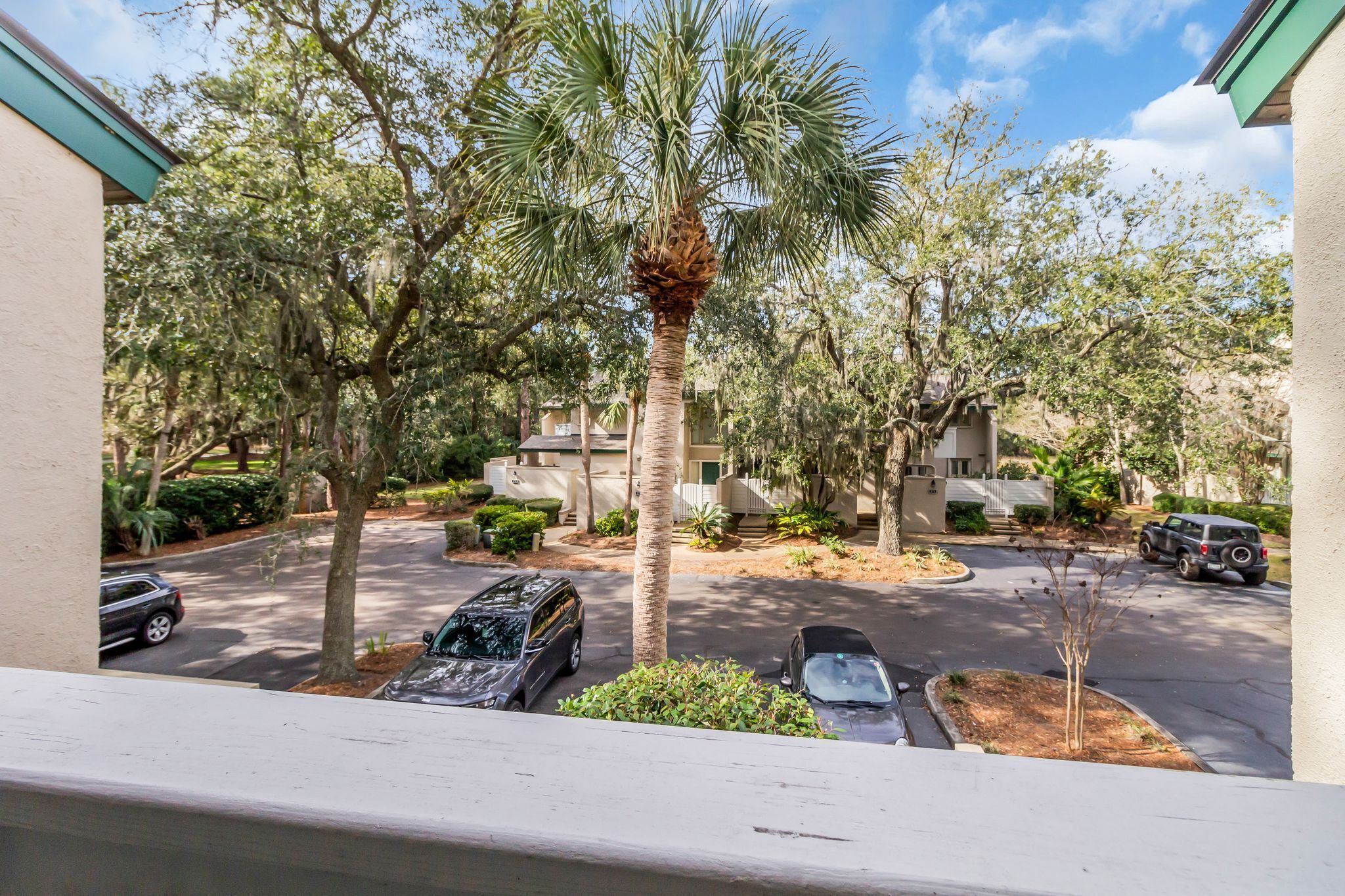 A residential area with parked cars, a palm tree, and houses with beige exteriors.