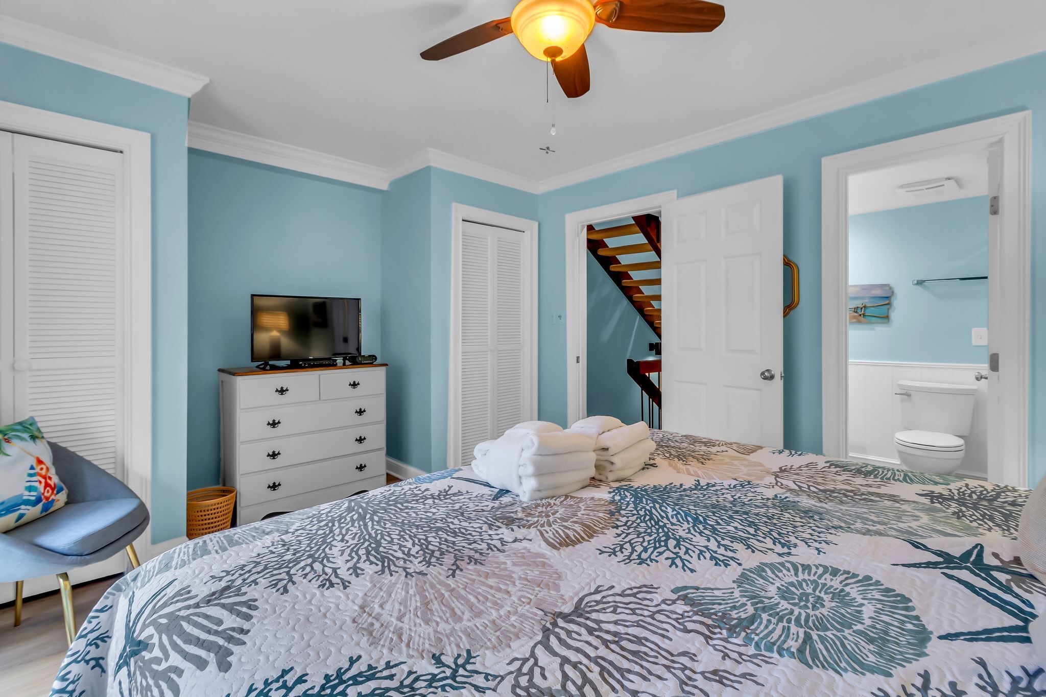 A bedroom with a bed, a TV, a dresser, a chair, and a ceiling fan.