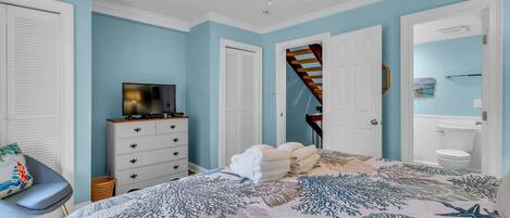 A bedroom with a bed, a TV, a dresser, a chair, and a ceiling fan.