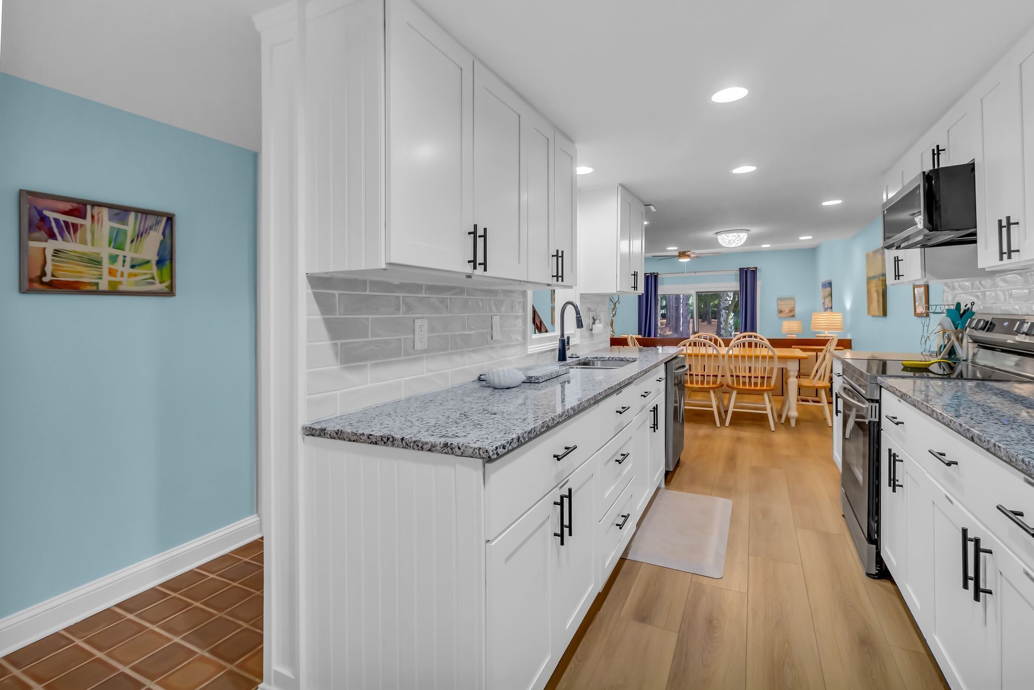 A modern kitchen with white cabinets, granite countertops, and a dining area with wooden chairs and a table.
