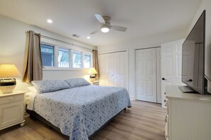Une chambre à coucher comprenant un lit, des tables de chevet, un ventilateur de plafond, une télévision et une armoire.