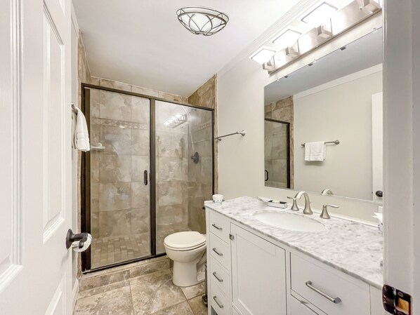 A modern bathroom with a glass-enclosed shower, a white toilet, and a marble countertop with a sink and vanity. - 895 Ketch Court at The Sea Pines Resort (Hilton Head Island)