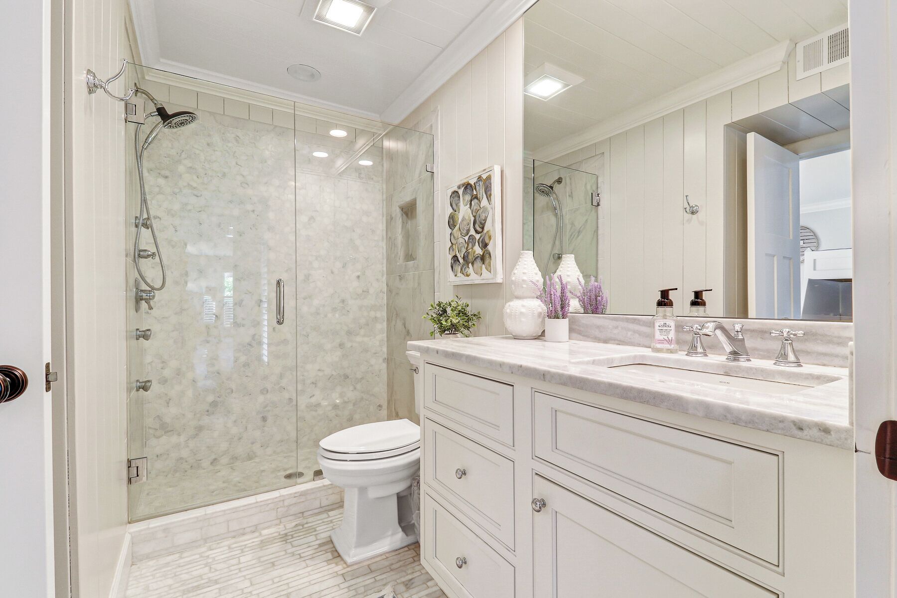 A modern bathroom with a glass-enclosed shower, a white toilet, and a marble countertop with a sink and vanity.