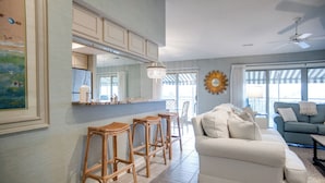Ein modernes Wohnzimmer mit einem weißen Sofa, einer Essecke mit Barhocker, einem großen Spiegel und einem Deckenventilator.
