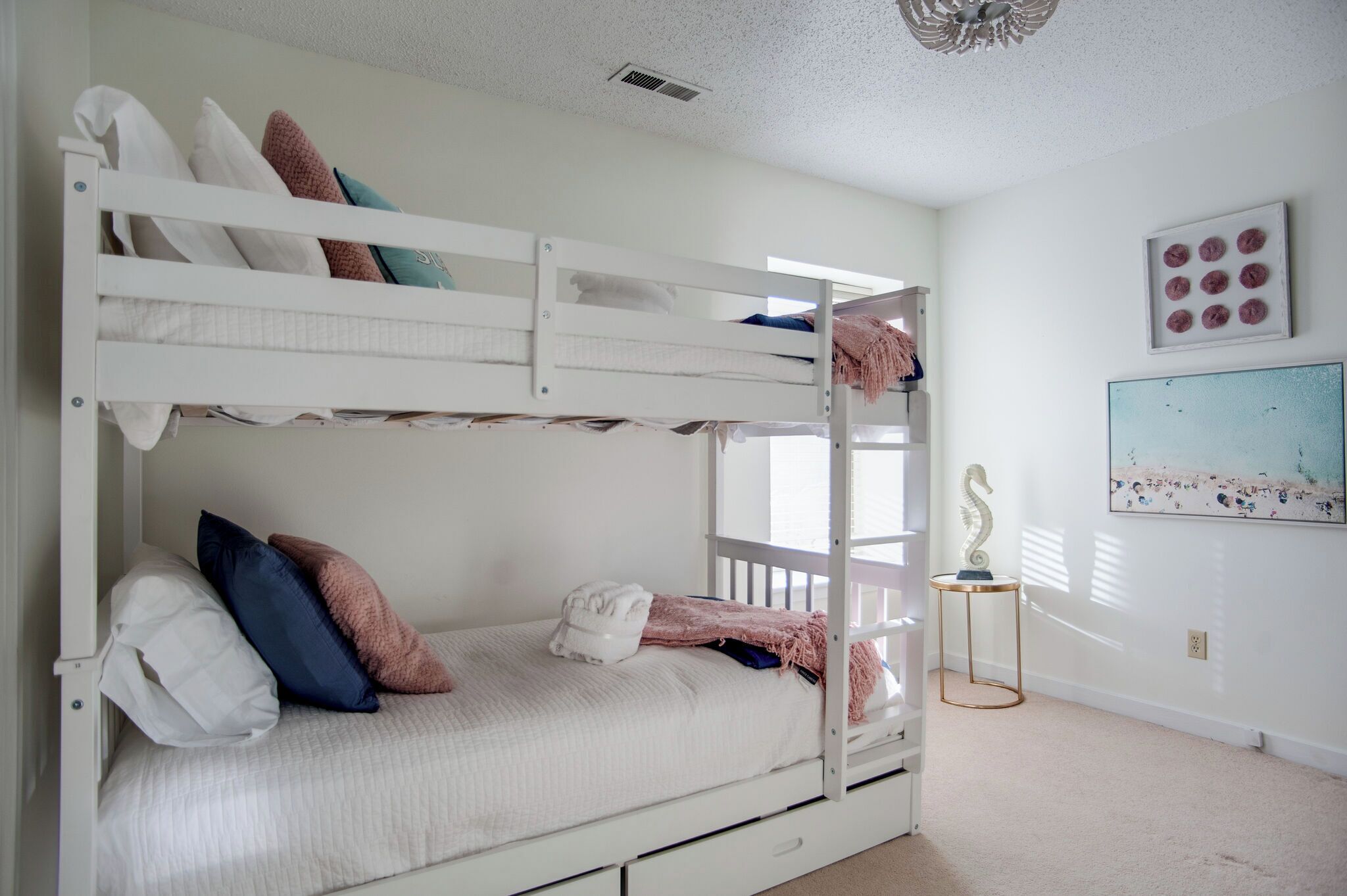 A bunk bed in a room with a white wall, a framed picture, and a small table with a decorative item.