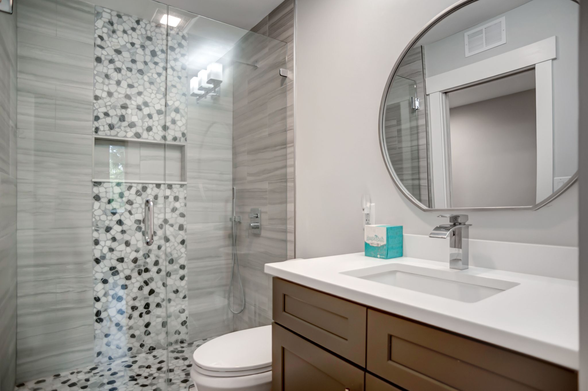 A modern bathroom with a glass shower enclosure, a white toilet, a sink with a mirror, and a box of Dove soap.