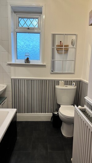 A bathroom with a striped wall, a window with a view, a toilet, and a radiator. - 2 Bedroom House in Manchester (Failsworth)