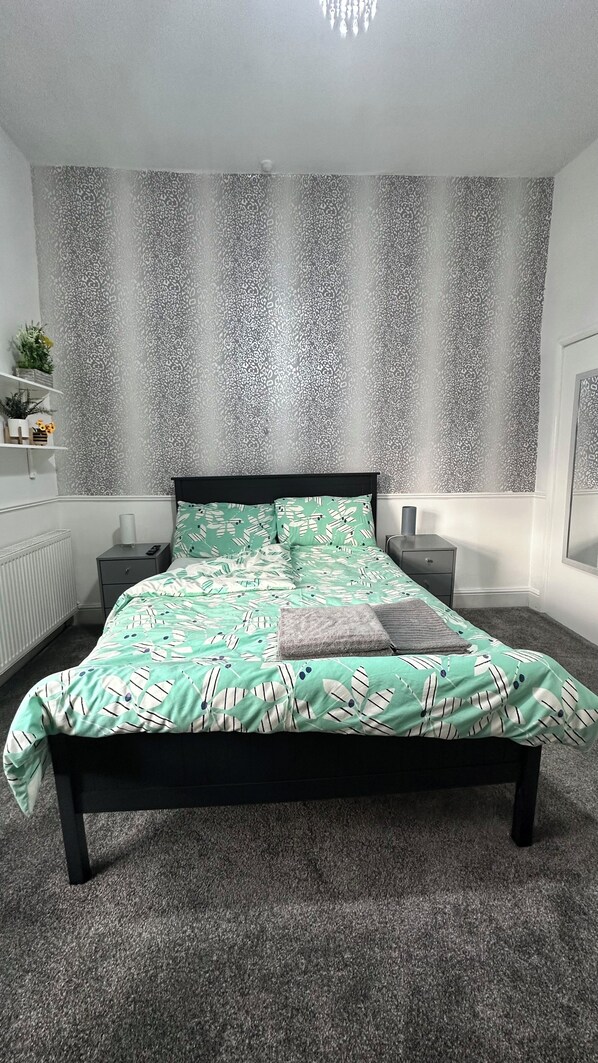 A bedroom with a bed, nightstands, a dresser, a radiator, and patterned wallpaper. - 2 Bedroom House in Manchester (Failsworth)