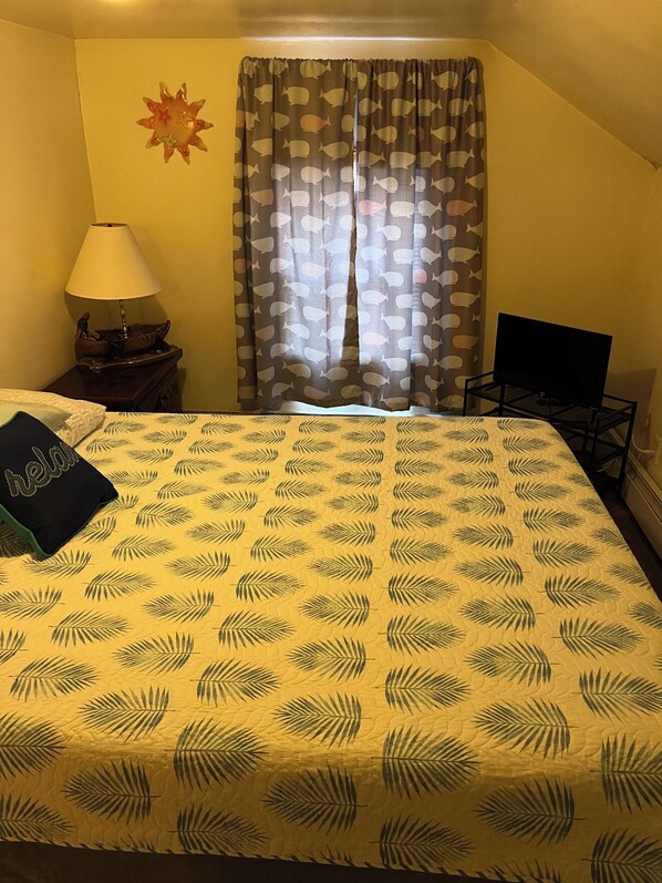 Une chambre d’hôtel avec un lit, une table de chevet avec une lampe, une télévision et une fenêtre avec des rideaux.