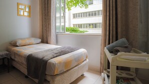 Une chambre à coucher avec un lit, une table de chevet, une fenêtre avec des rideaux et une vue sur un bâtiment à l’extérieur.