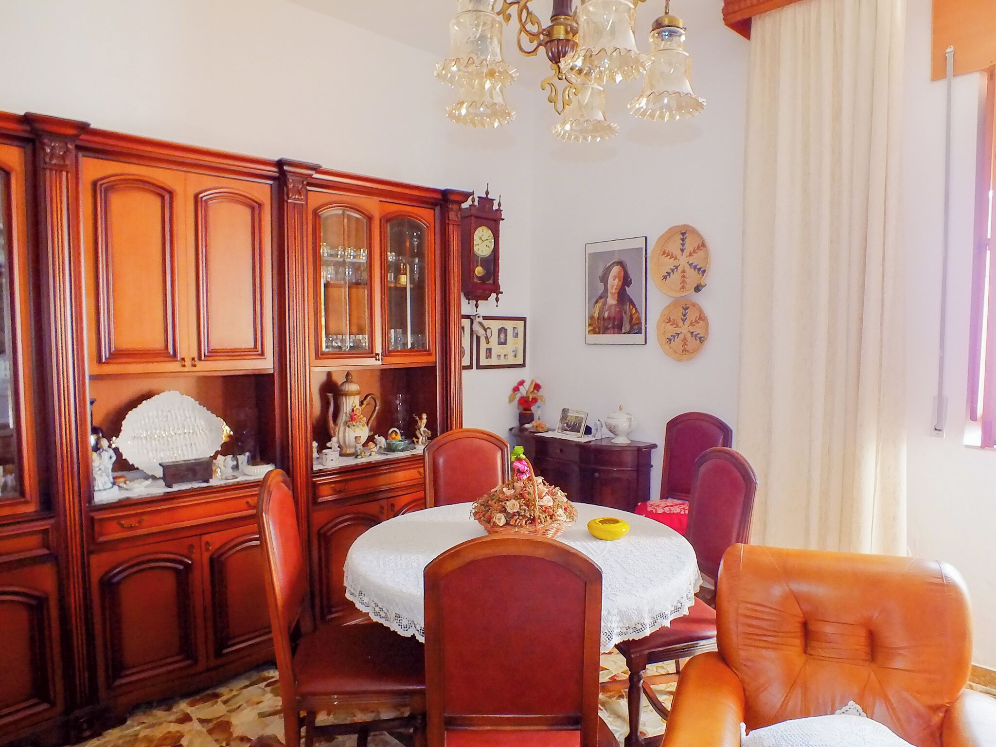 A dining area with a wooden cabinet, a table with a lace tablecloth, and a chandelier.