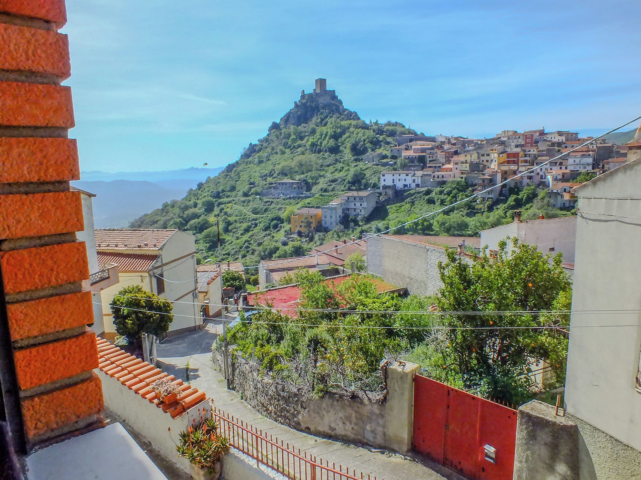 A hillside town with traditional buildings, a prominent castle-like structure, and a red fence in the foreground.