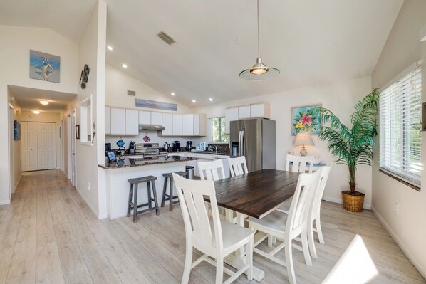 A spacious kitchen with white cabinets, a central island, and a dining area with white chairs.