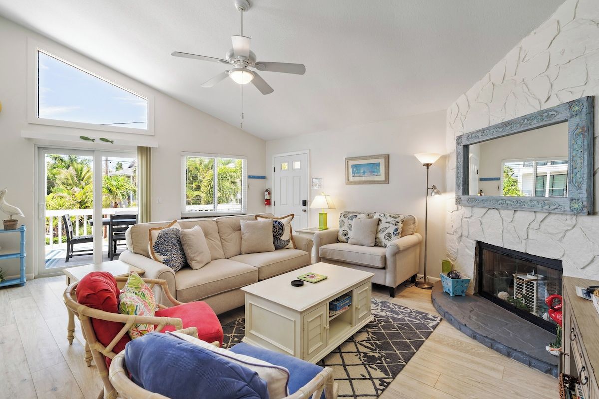 A spacious living room with a high ceiling, a fireplace, and a balcony with outdoor furniture.