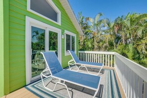 Een groen gebouw met een balkon, twee loungestoelen en uitzicht op palmbomen.