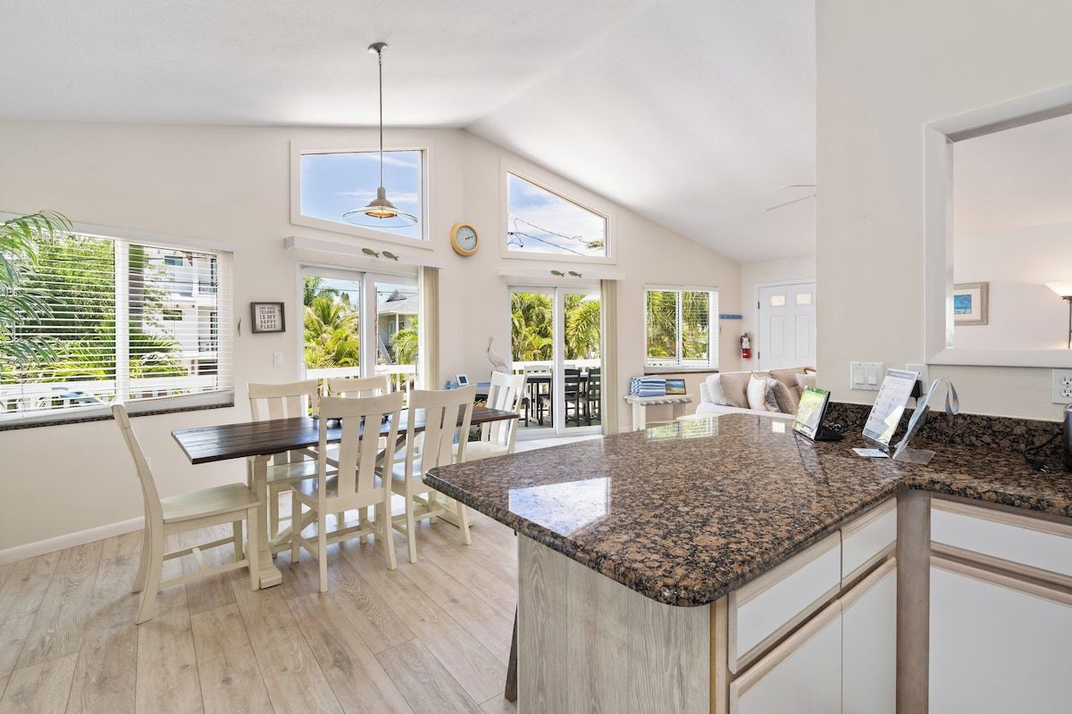 A spacious kitchen with a granite countertop, white cabinetry, and a dining area with white chairs.