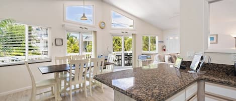 A spacious kitchen with a granite countertop, white cabinetry, and a dining area with white chairs.