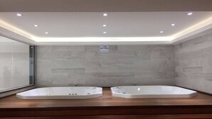 Un baño moderno con dos bañeras separadas, un tocador de madera y cabina de ducha con mampara de vidrio.