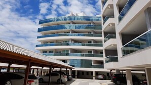 Un edificio de varios pisos con balcones, una zona de estacionamiento techada y un cielo despejado.