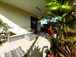 A sunlit patio with a sofa, wicker furniture, and potted plants.