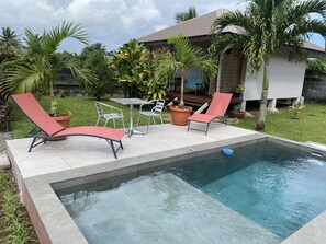 A swimming pool with lounge chairs and a table, surrounded by potted plants and a house. - Tahiti - Bungalow Toah Piti (Taiarapu-Ouest)