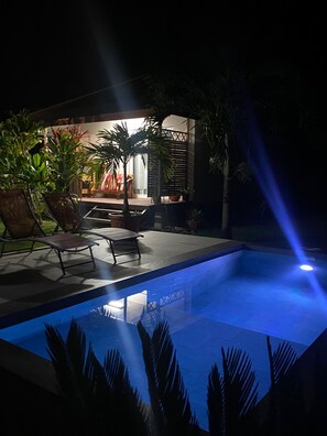 A swimming pool with a blue-lit edge, surrounded by lounge chairs and potted plants. - Tahiti - Bungalow Toah Piti (Taiarapu-Ouest)
