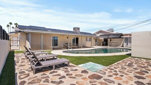 A residential property with a swimming pool, lounge chairs, and solar panels on the roof.
