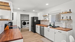 A modern kitchen with white cabinets, a wooden countertop, a black refrigerator, and a built-in washing machine.