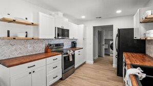 A modern kitchen with white cabinets, wooden countertops, a built-in oven, and a microwave.
