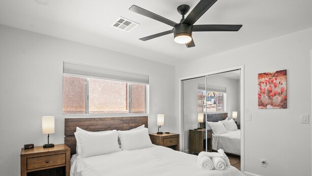 A bedroom with a bed, nightstands, a ceiling fan, a window, and a mirror.