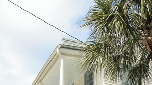 Un edificio de dos pisos con balcón, una puerta azul y una palmera.