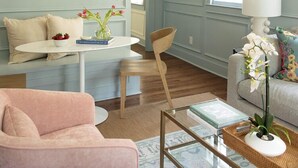Un salón con un sofá, una mesa de centro y un sillón. Hay un cuadro en la pared y una ventana con cortinas.
