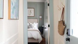 Un pasillo que conduce a un dormitorio con cama, una cesta colgante y un candelabro.